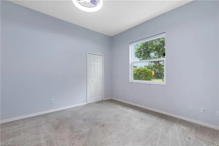 Bright interior space featuring light blue walls, gray carpeting, a large window providing natural light, a white bi-fold closet door, and a modern ceiling fixture