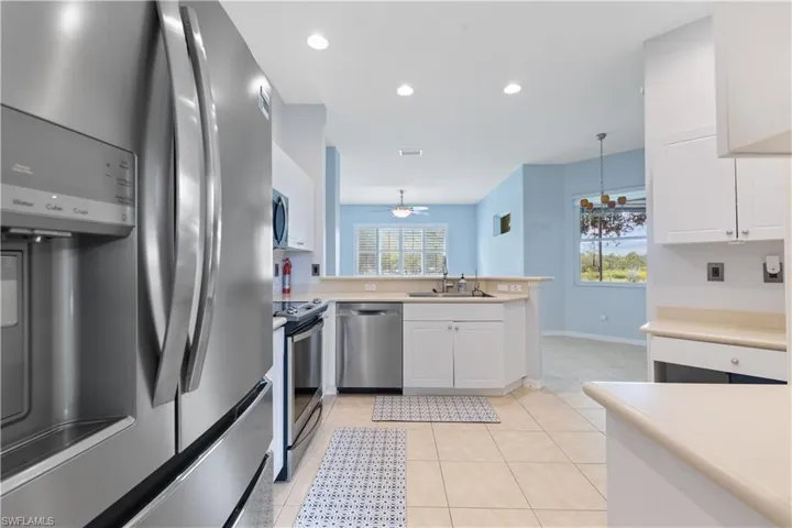 Kitchen featuring stainless steel appliances, white cabinetry, light-toned countertops, tile flooring, and recessed lighting
