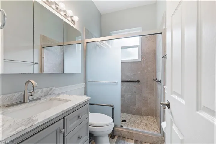 Contemporary bathroom featuring a walk-in shower with tiled walls and a pebble floor, a vanity with a white-veined countertop and an undermount sink, a large mirrored medicine cabinet, and wood-finish flooring