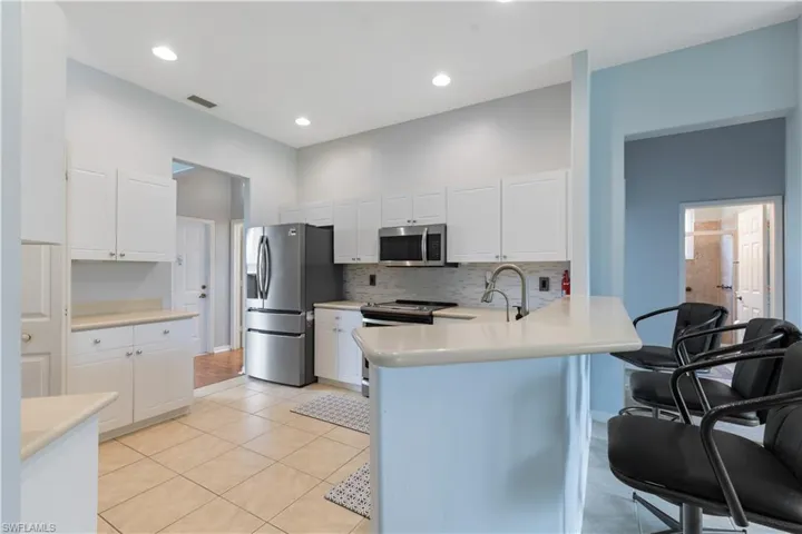 Kitchen featuring white shaker cabinetry, stainless steel appliances, a white subway tile backsplash, and a breakfast bar with a light-toned countertop