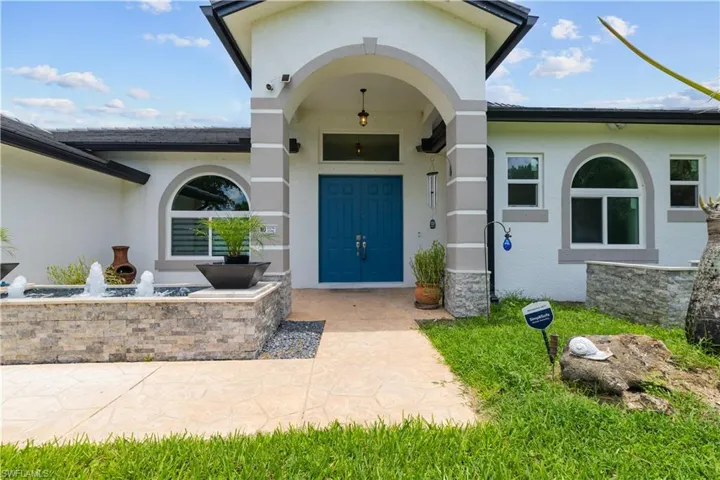 Stucco exterior with a prominent arched entry, dual blue entry doors, an integrated water feature with stone-finish cladding, arched windows, and a stamped concrete walkway