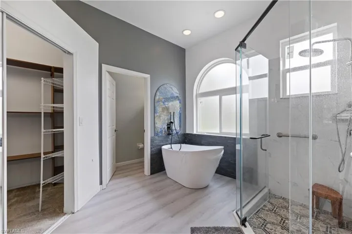 Contemporary bathroom with a freestanding tub, glass-enclosed shower, arched window, and wood-finish flooring