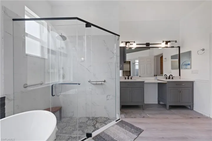 Spacious bathroom featuring a glass-enclosed shower with a rainfall showerhead, white marble-look tile, and decorative floor tiling