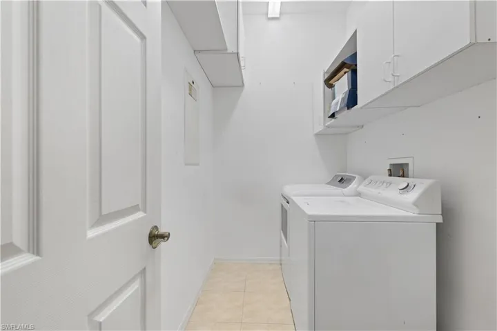 Dedicated laundry area featuring tile flooring, white cabinetry, and upper shelving