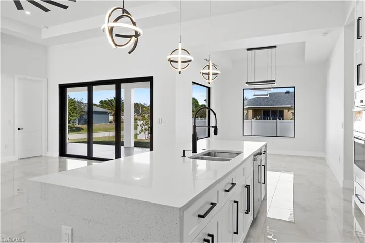 Kitchen with a raised ceiling, sink, a kitchen island with sink, and decorative light fixtures