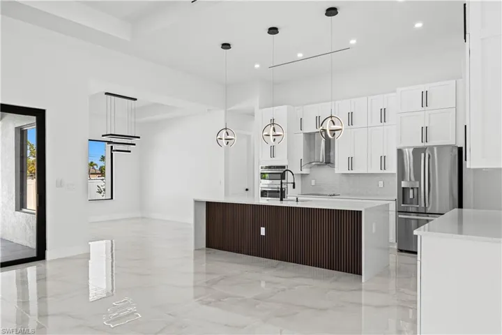 Kitchen with white cabinetry, hanging light fixtures, a center island with sink, stainless steel appliances, and backsplash