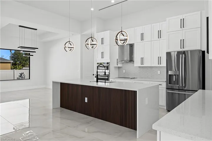 Kitchen featuring wall chimney exhaust hood, a center island with sink, hanging light fixtures, stainless steel appliances, and white cabinets