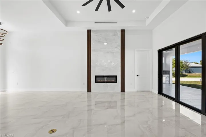 Unfurnished living room featuring a tray ceiling, a fireplace, and ceiling fan