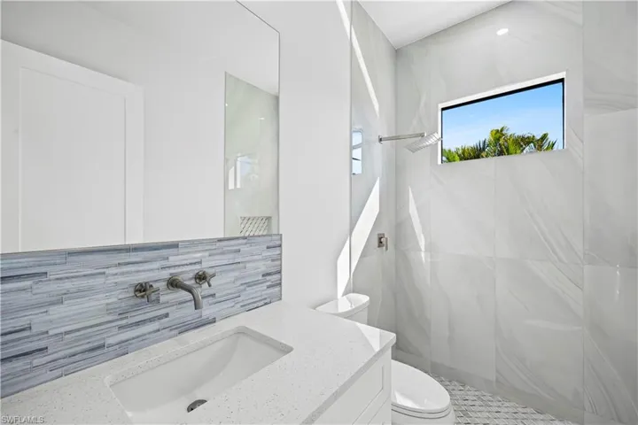 Bathroom featuring vanity, a tile shower, backsplash, and toilet