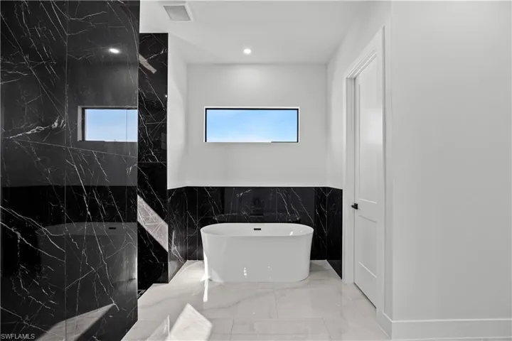 Bathroom featuring tile walls, a tub to relax in, and a wealth of natural light
