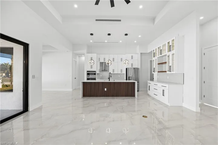 Kitchen with appliances with stainless steel finishes, backsplash, white cabinets, a center island with sink, and decorative light fixtures