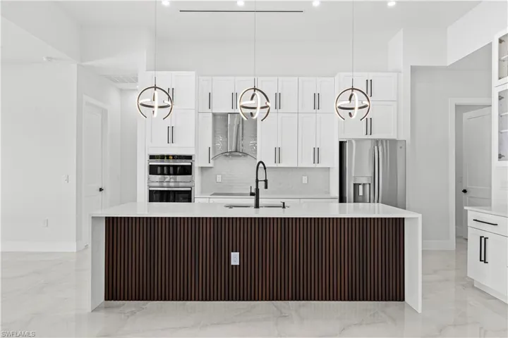 Kitchen featuring wall chimney range hood, sink, an island with sink, and appliances with stainless steel finishes