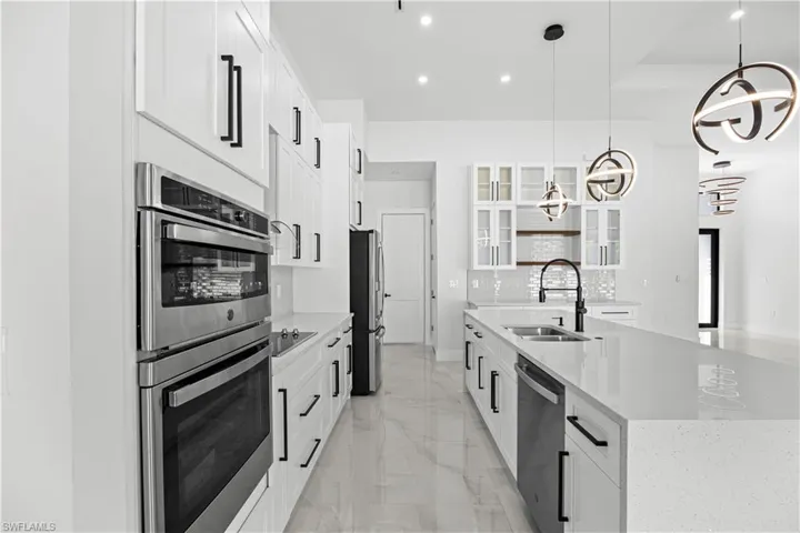 Kitchen with pendant lighting, white cabinetry, stainless steel appliances, and an island with sink