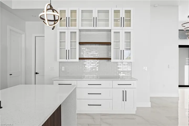 Kitchen featuring white cabinetry, backsplash, light stone countertops, and pendant lighting