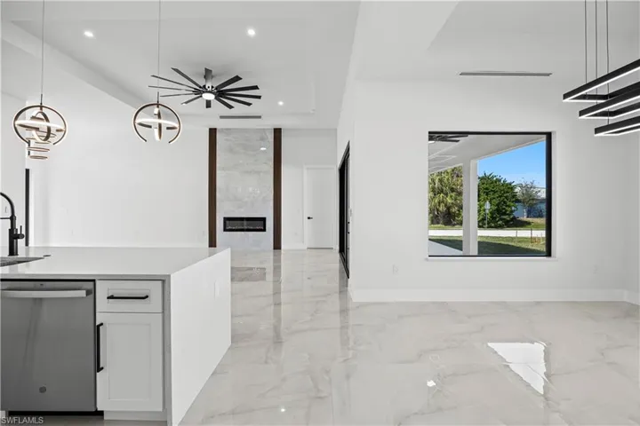 Kitchen with dishwasher, sink, white cabinets, hanging light fixtures, and a high end fireplace