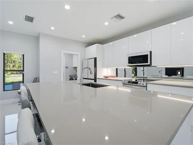 Kitchen featuring a kitchen bar, white cabinetry, light stone counters, a large island with sink, and recessed lighting