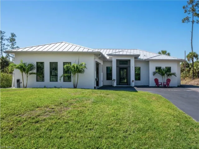 View of front facade with a standing seam roof, stucco siding, and a front lawn