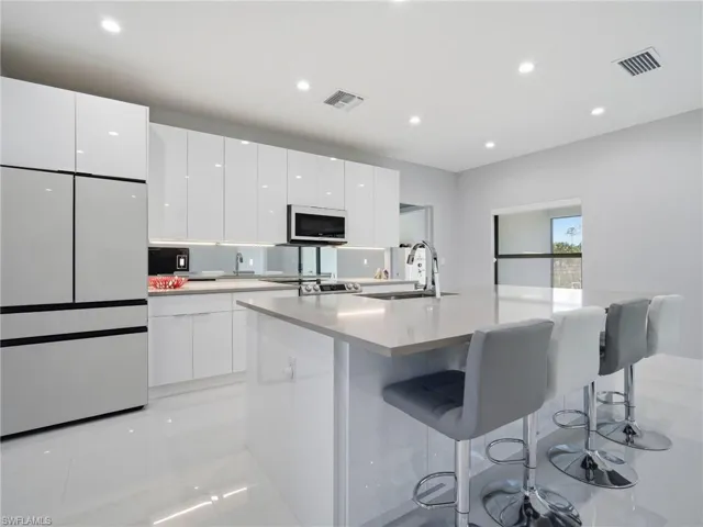 Kitchen with white appliances, a center island with sink, white cabinets, a kitchen breakfast bar, and modern cabinets