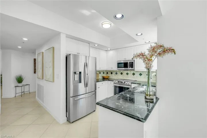 Kitchen with stainless steel appliances, tasteful backsplash, white cabinets, light tile patterned floors, and recessed lighting