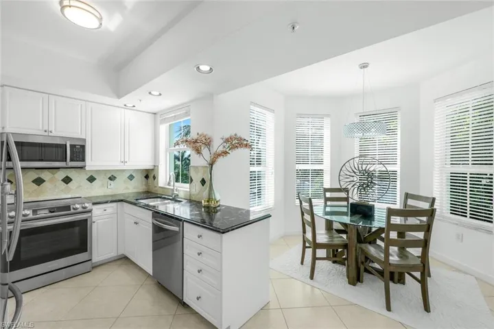 Kitchen with dark stone counters, recessed lighting, stainless steel appliances, light tile patterned floors, and white cabinets