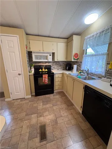 Kitchen with sink, backsplash, cream cabinets, and black appliances