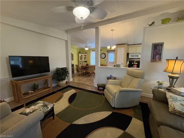 Living room featuring ceiling fan with notable chandelier, lofted ceiling with beams, and hardwood / wood-style flooring