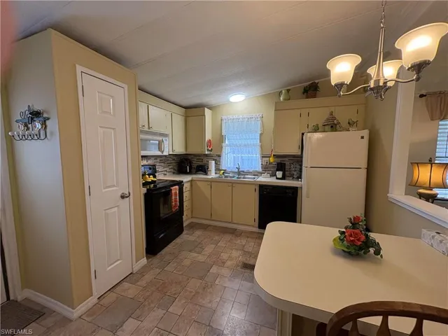 Kitchen with sink, black appliances, hanging light fixtures, cream cabinets, and backsplash