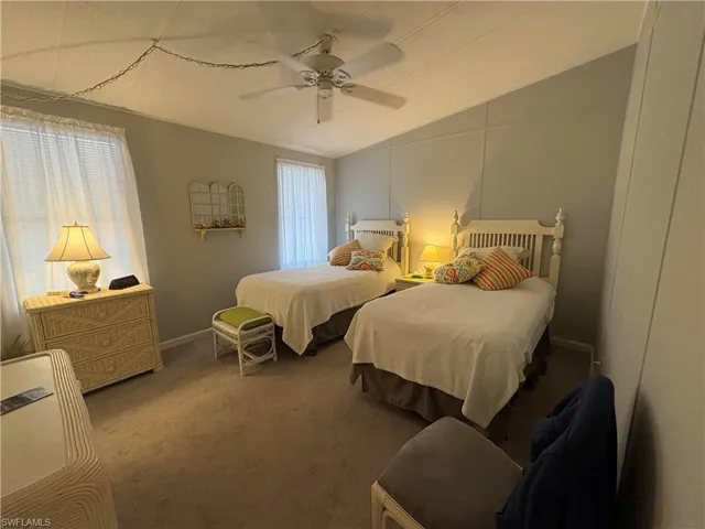 Carpeted bedroom featuring multiple windows, vaulted ceiling, and ceiling fan