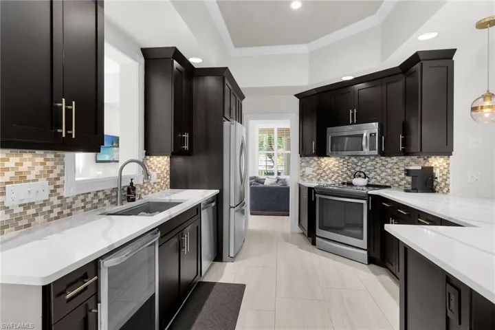 Kitchen with appliances with stainless steel finishes, light stone countertops, tasteful backsplash, hanging light fixtures, and crown molding