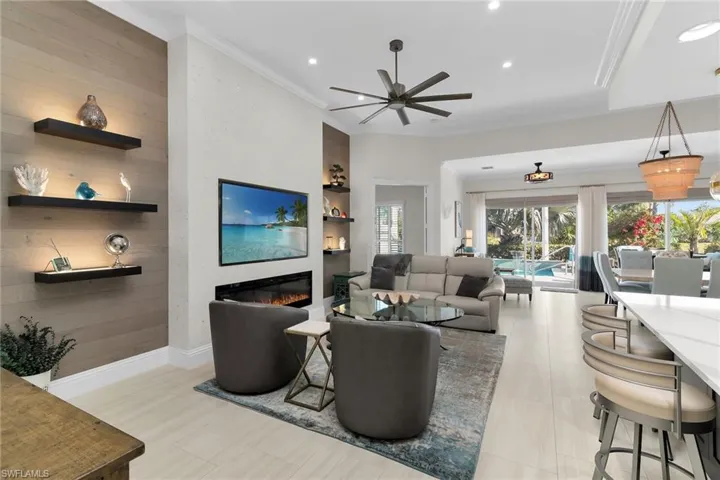 Living room featuring a glass covered fireplace, built in features, ceiling fan, ornamental molding, and recessed lighting