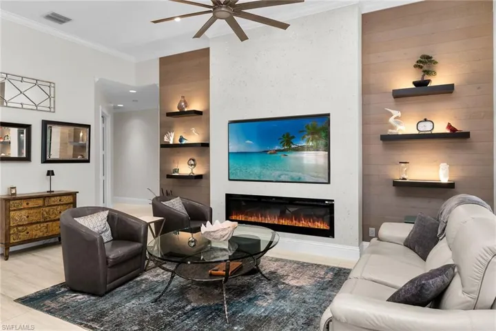 Living area with built in features, a glass covered fireplace, ornamental molding, and a ceiling fan