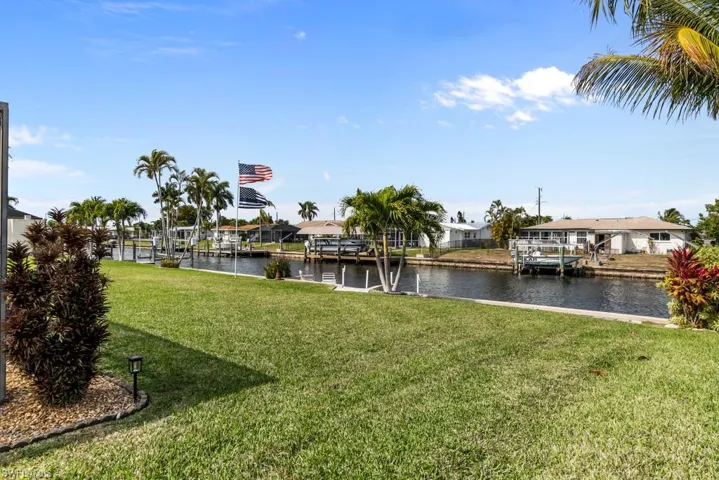 Dock area with a water view, boat lift, a yard, and a residential view
