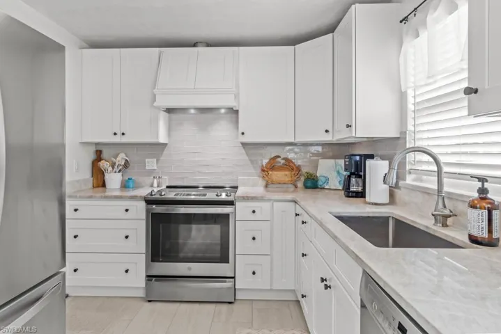 Kitchen with stainless steel appliances, white cabinetry, and light stone counters