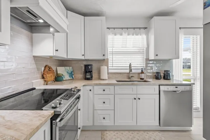 Kitchen featuring stainless steel appliances, white cabinets, and light stone counters