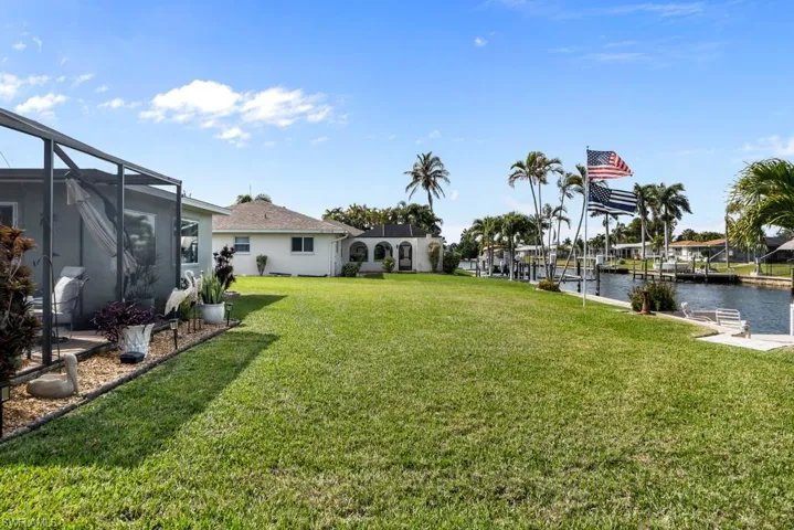View of green lawn featuring a lanai, a water view, a sunroom, and a boat dock
