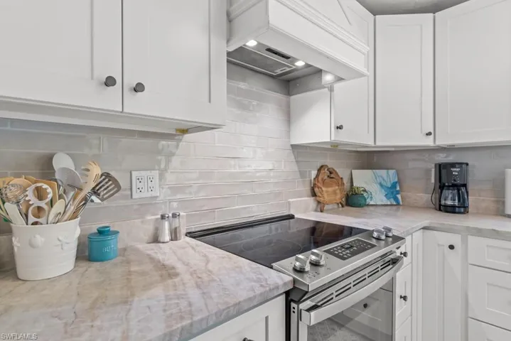 Kitchen featuring electric range, white cabinetry, backsplash, and light stone counters