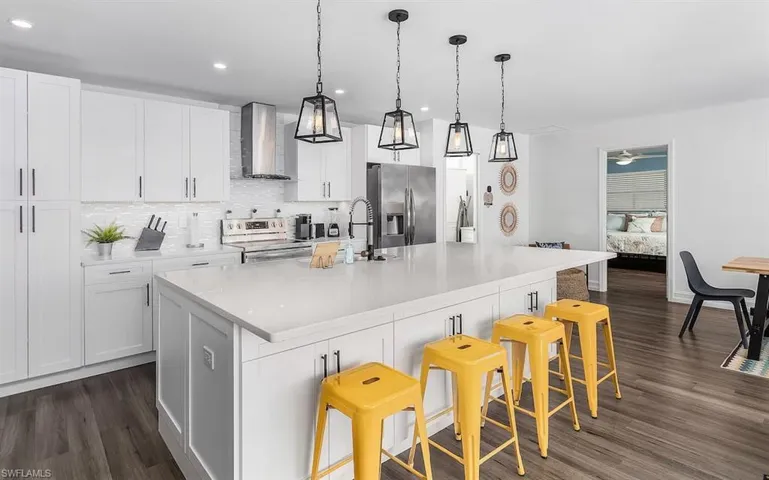 Kitchen with white cabinets, appliances with stainless steel finishes, dark wood-type flooring, wall chimney range hood, and backsplash