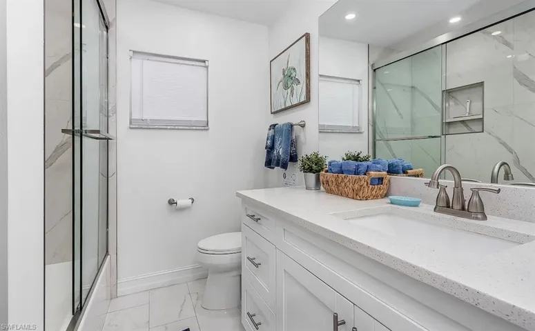 Bathroom with toilet, marble finish floor, a marble finish shower, and vanity