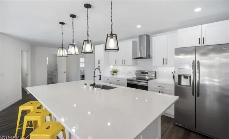 Kitchen with backsplash, appliances with stainless steel finishes, a sink, an island with sink, and wall chimney exhaust hood