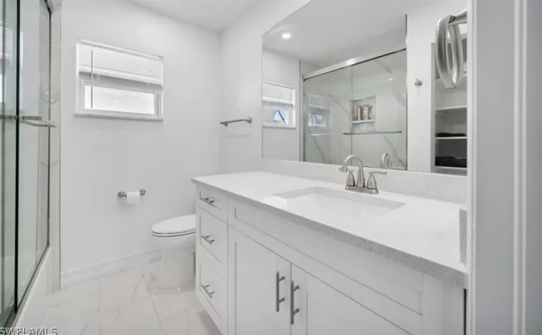 Full bath with toilet, vanity, baseboards, marble finish floor, and a marble finish shower
