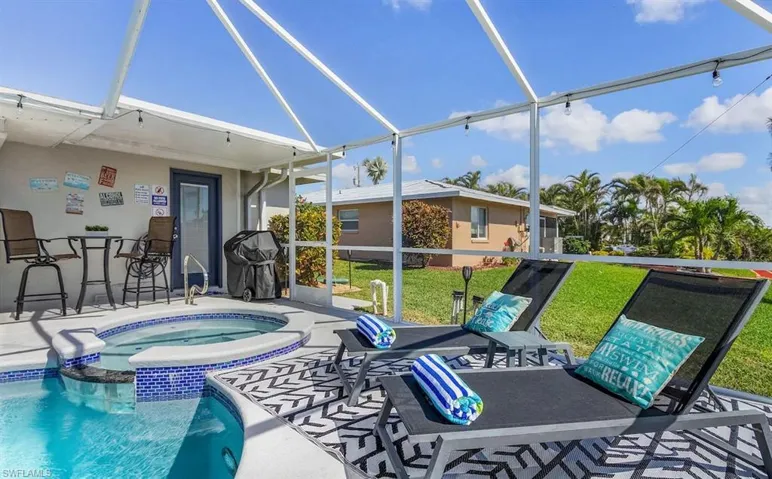 View of pool featuring outdoor dry bar, a pool with connected hot tub, a lawn, glass enclosure, and a patio area