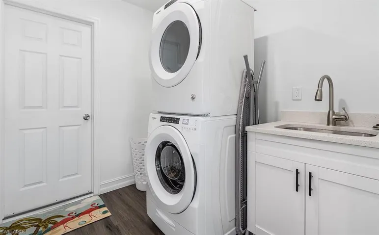 Laundry area with dark wood-type flooring, a sink, baseboards, stacked washer / drying machine, and cabinet space
