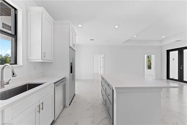 Kitchen side view featuring stainless steel dishwasher, sink, a center island, white cabinetry, and white fridge with ice dispenser