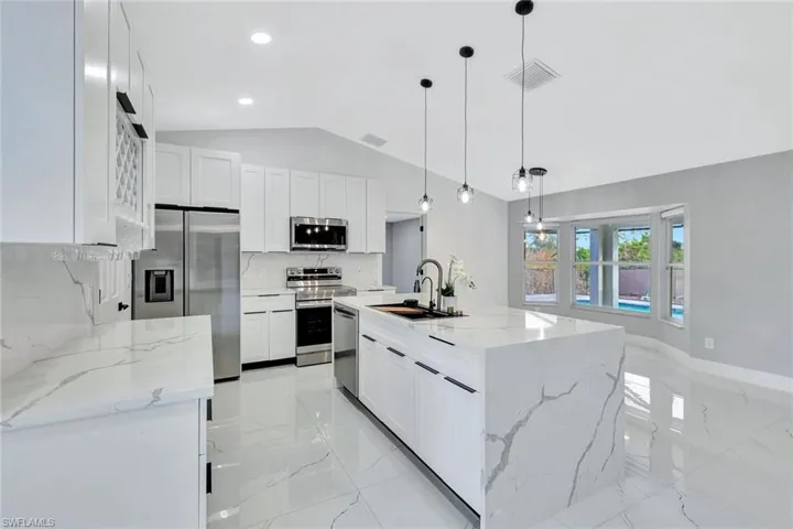 Kitchen featuring stainless steel appliances, white cabinets, marble finish floor, a center island with sink, and pendant lighting