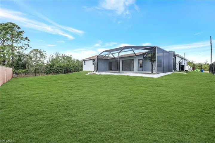 Back of house with glass enclosure, a lawn, fence, and a patio