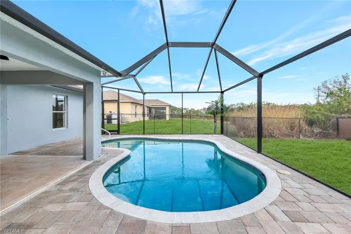 View of swimming pool featuring glass enclosure, a fenced in pool, a lawn, and a patio