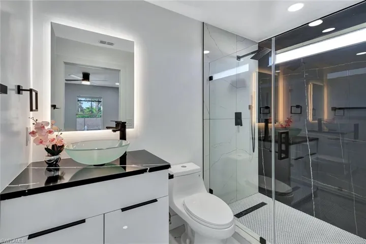 Full bath with a marble finish shower, visible vents, toilet, ceiling fan, and vanity