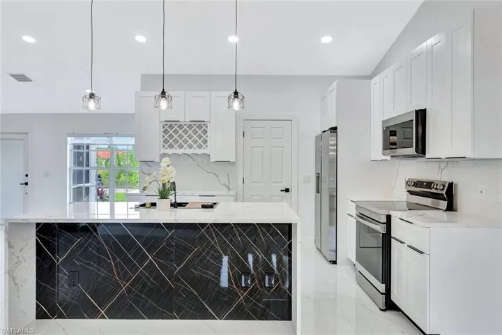 Kitchen featuring marble finish floor, stainless steel appliances, white cabinetry, and pendant lighting