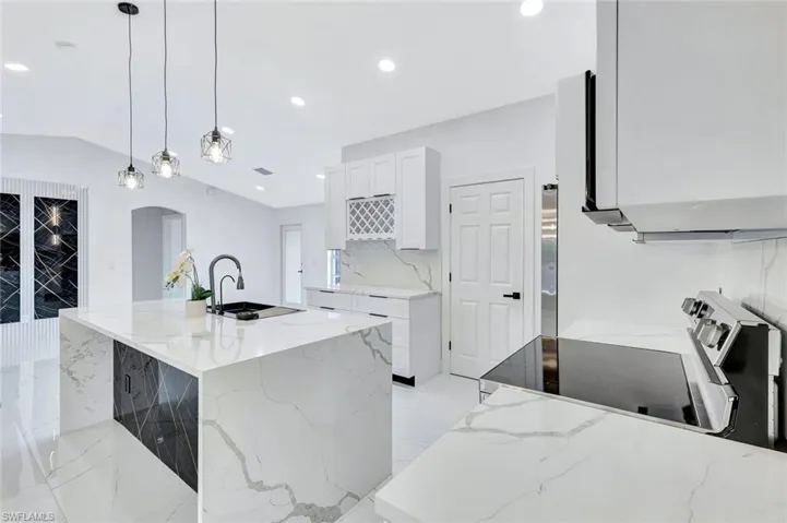 Kitchen featuring pendant lighting, white cabinetry, an island with sink, and light stone countertops
