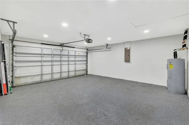 Garage with concrete block wall, electric panel, a garage door opener, and electric water heater